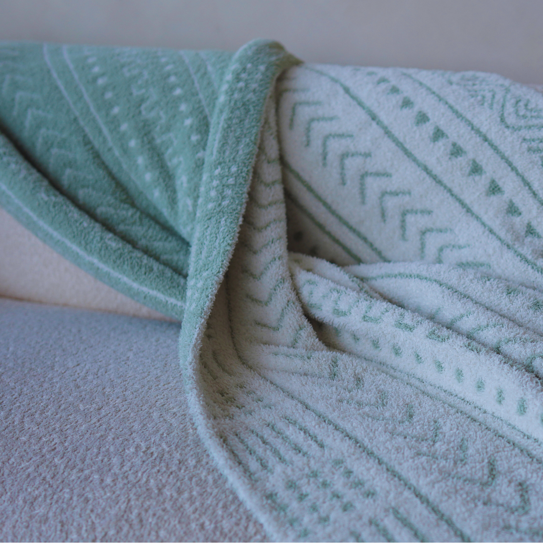 Close-up of a soft mint green and white patterned throw blanket draped over a textured cream sofa, showcasing intricate woven details