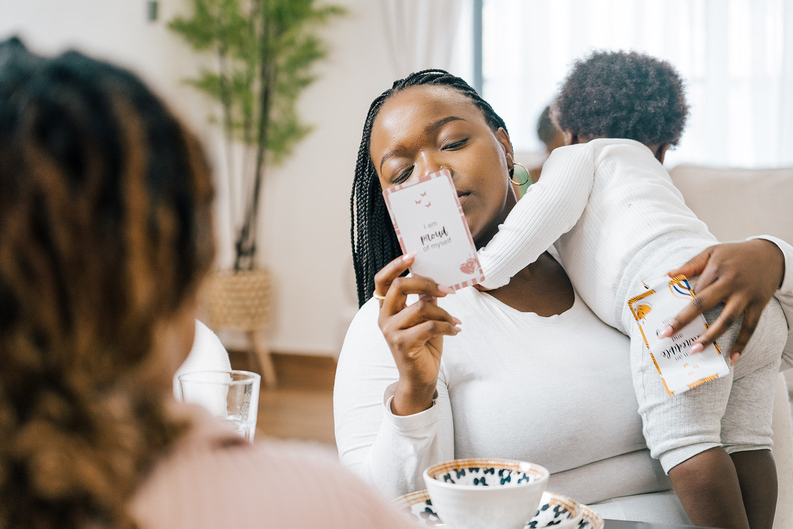 Black mother holding her baby while reading affirmation cards that say 'I am proud of myself' during a mindful moment at the table