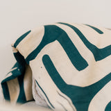 Close-up of a folded cream and dark green abstract-patterned fabric draped over a couch in a minimalist living space