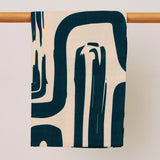 Modern textile with abstract dark green brushstroke pattern hanging on a wooden rod against a neutral background