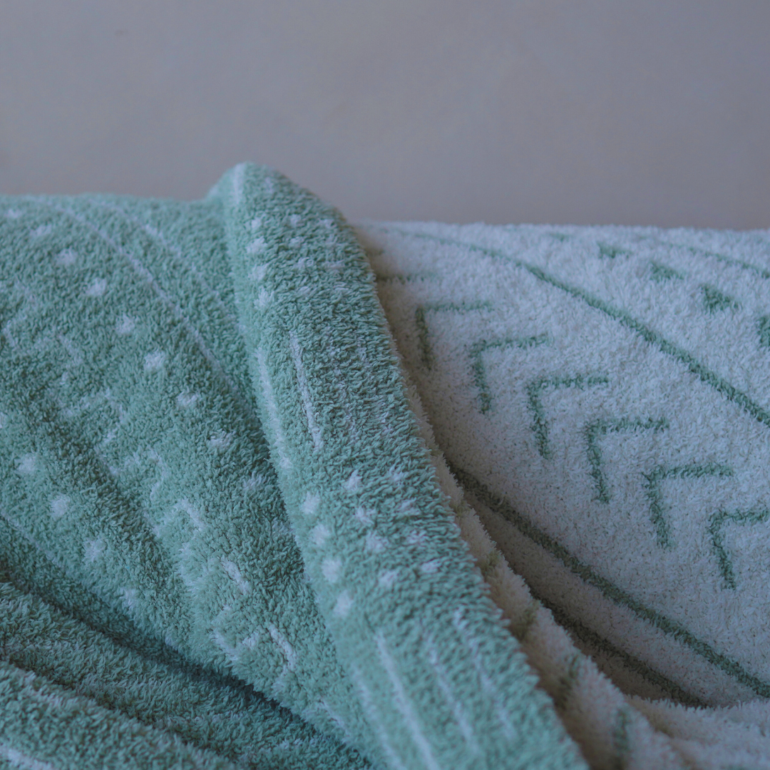 Close-up of a soft mint green and white patterned throw blanket draped over a textured cream sofa, showcasing intricate woven details