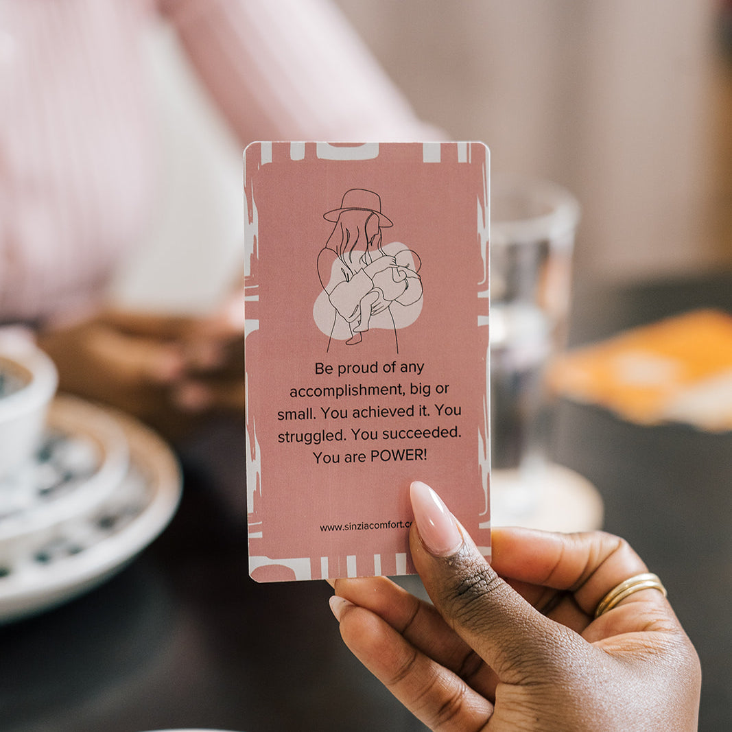 Close-up of a hand holding an affirmation card that reads 'Be proud of any accomplishment...' during a moment of encouragement at the dining table